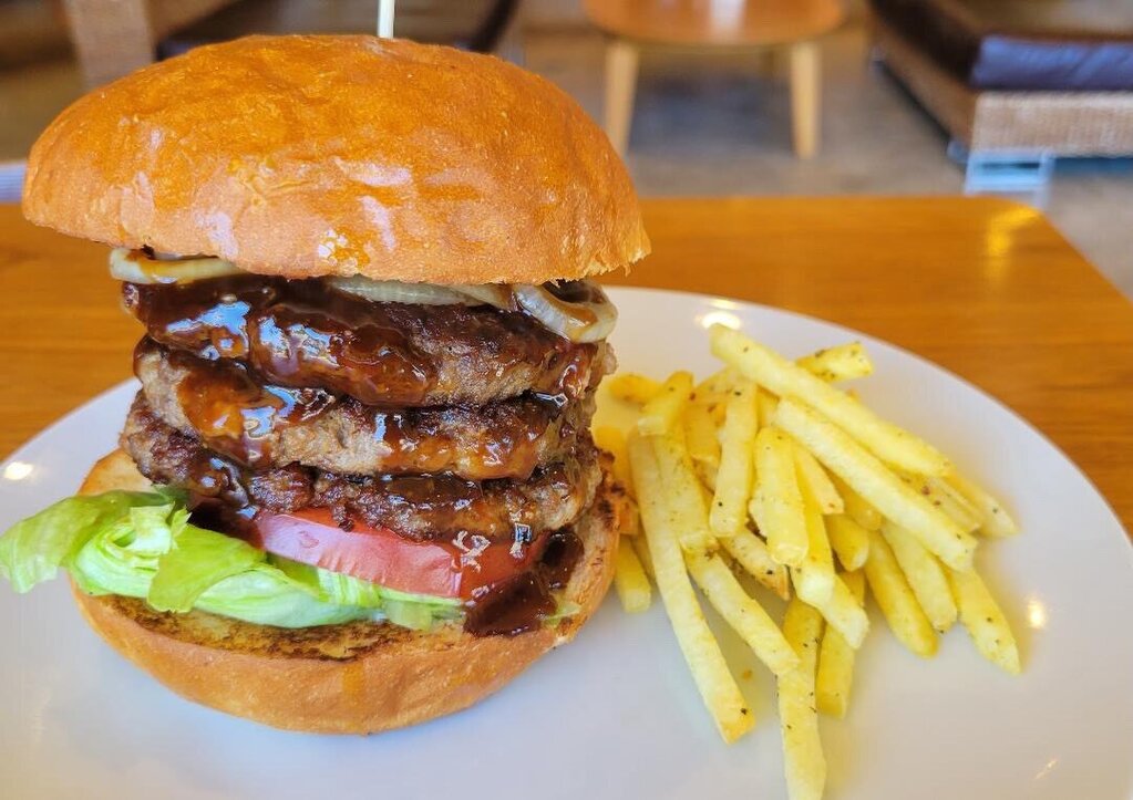 パティを何層にも重ね照り焼きソースをかけたa・la・Domoのボリューム満点バーガー。フライドポテトが添えられている（a・la・Domo公式Instagramより）