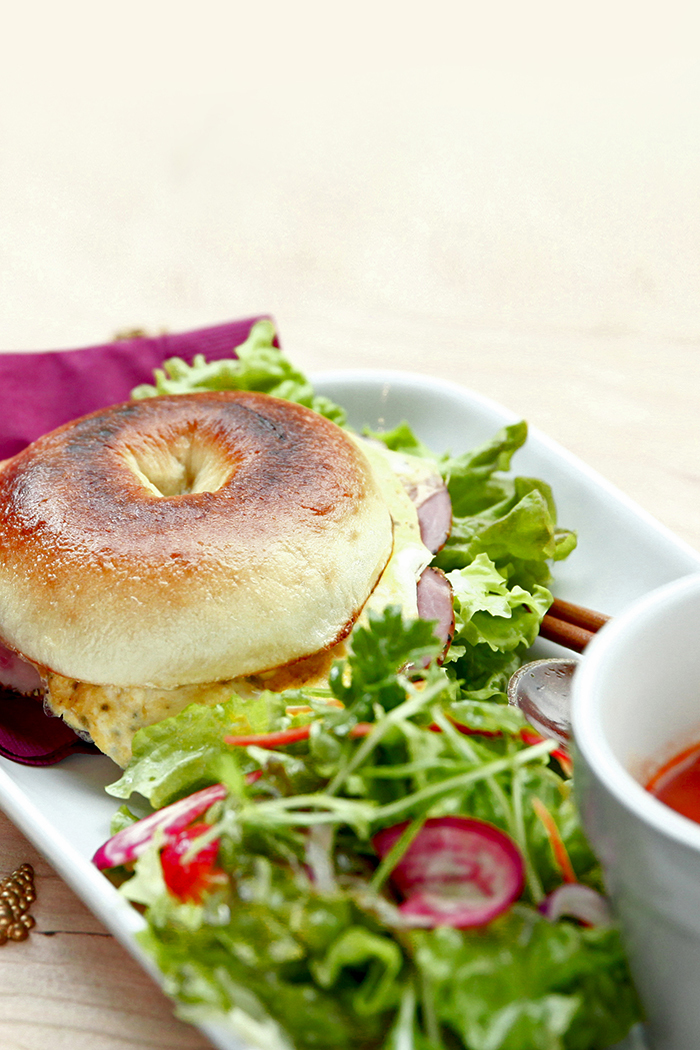 こんがり焼いたベーグルに卵とハムをはさんだホットサンド、たっぷりのグリーンサラダとスープを白い皿に盛り付けたランチセット(アンティーク&オールディーズ公式サイトより)