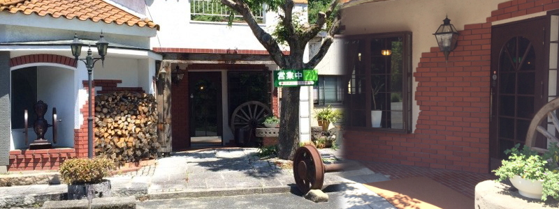 赤い瓦屋根と白い壁、レンガの入口に「営業中」の看板と薪の束、車輪のオブジェが並ぶカフェリーフの外観(カフェリーフ公式サイトより)