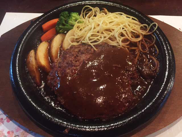 黒い鉄板の上でデミグラスソースがたっぷりかかったハンバーグに、パスタ、ポテト、にんじん、ブロッコリーが添えられている(カフェリーフ公式サイトより)