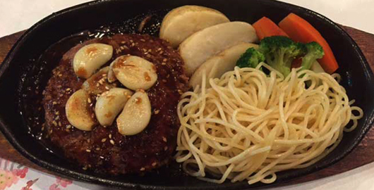 鉄板の上で、ごろっとしたにんにくとごまがのったスタミナハンバーグとパスタ、野菜の付け合わせ(カフェリーフ公式サイトより)