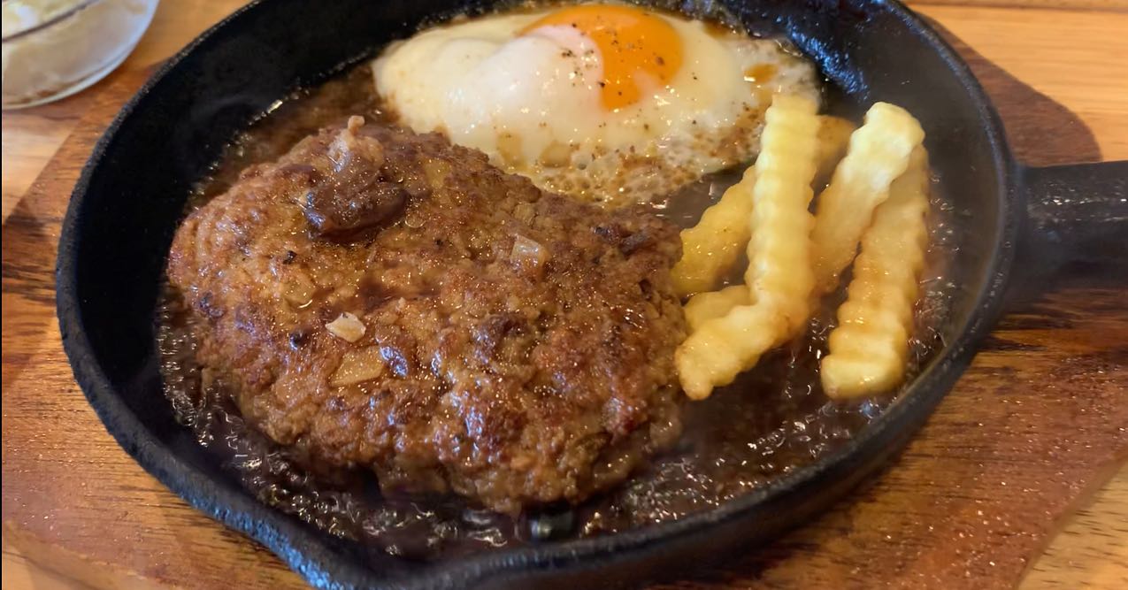 CAFE麓の鉄板焼きハンバーグ。スキレットにハンバーグと目玉焼き、波形のフライドポテトが並ぶ(公式Instagramより)