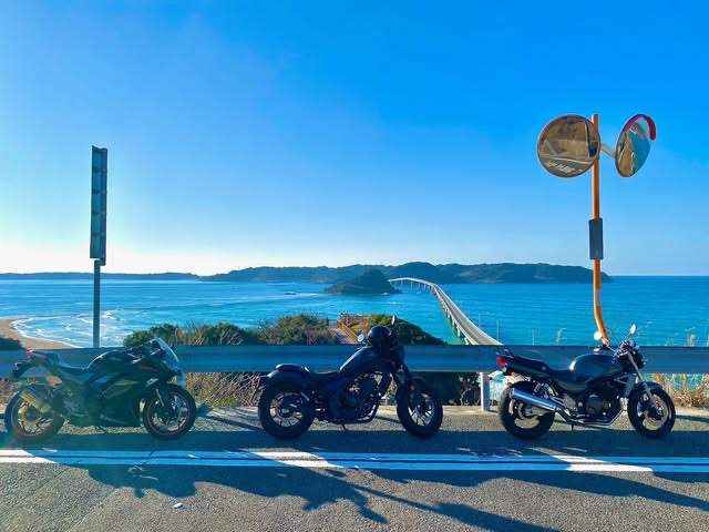 海沿いの道に3台のバイクが並び、背景に青い海と角島大橋が広がる晴れた日の風景（Goodies Ella公式Instagramより）