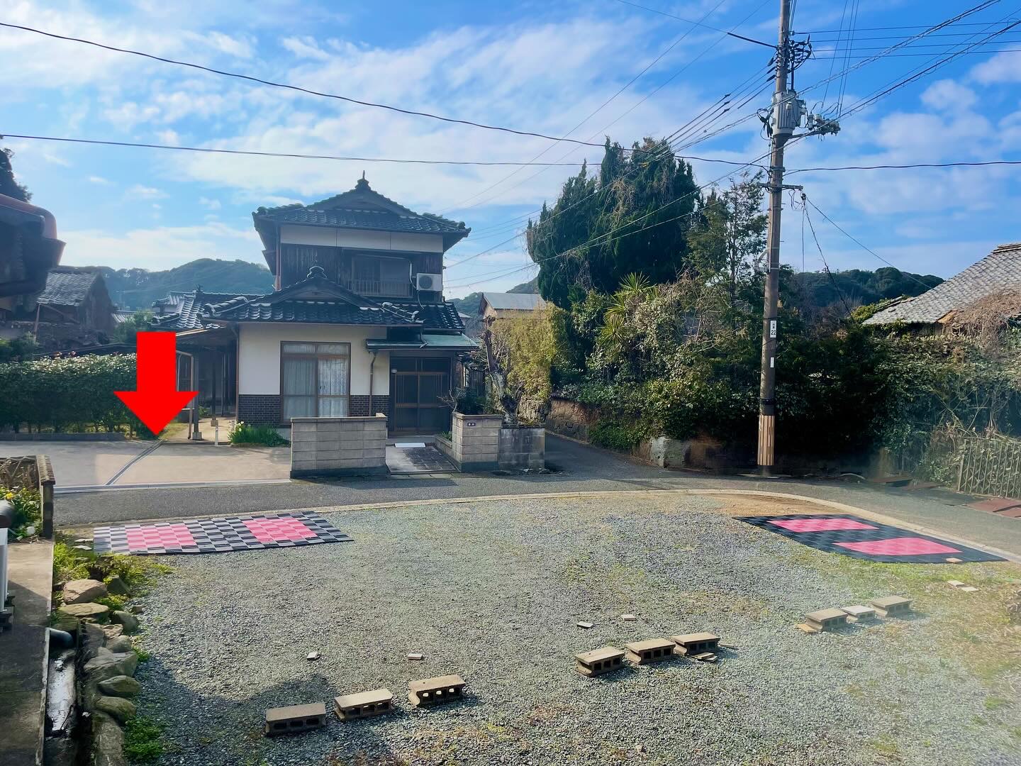 赤い矢印で示された、ピンクの目印と車止めが並ぶ砂利敷きの駐車スペースと、奥に見える瓦屋根の家並み（Goodies Ella公式Instagramより）