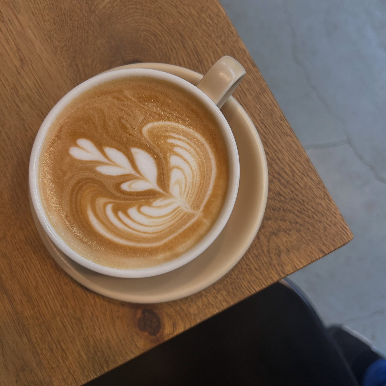 木のテーブルに置かれた、リーフのラテアートが描かれたホットラテ(The Little Coffee Stand公式Instagramより)