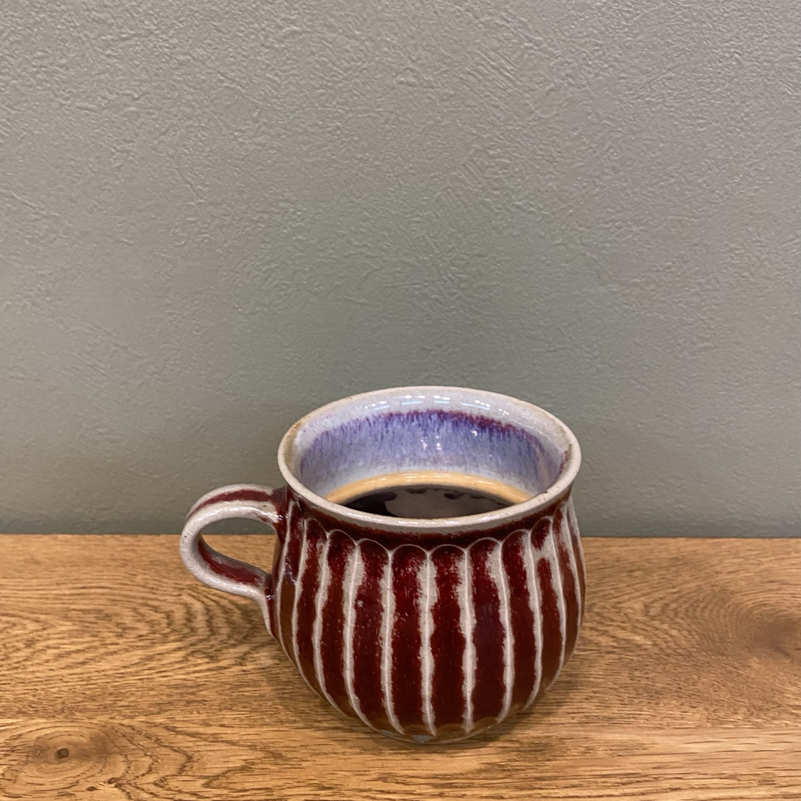 木のカウンターに置かれた、えんじ色と白のしのぎ模様のマグカップに入ったブラックコーヒー(The Little Coffee Stand公式サイトのメニューページより)