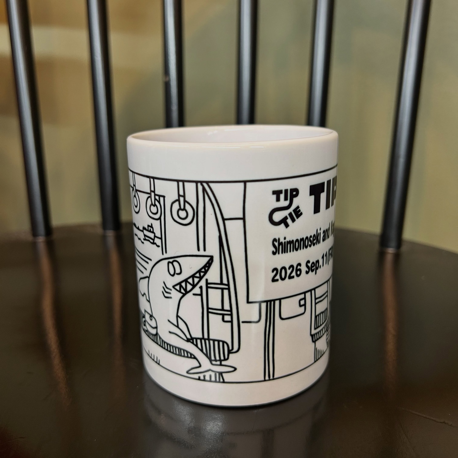 電車の車内とサメのイラストが描かれたTipTie 2026のオリジナルマグカップ(The Little Coffee Stand公式Instagramより)