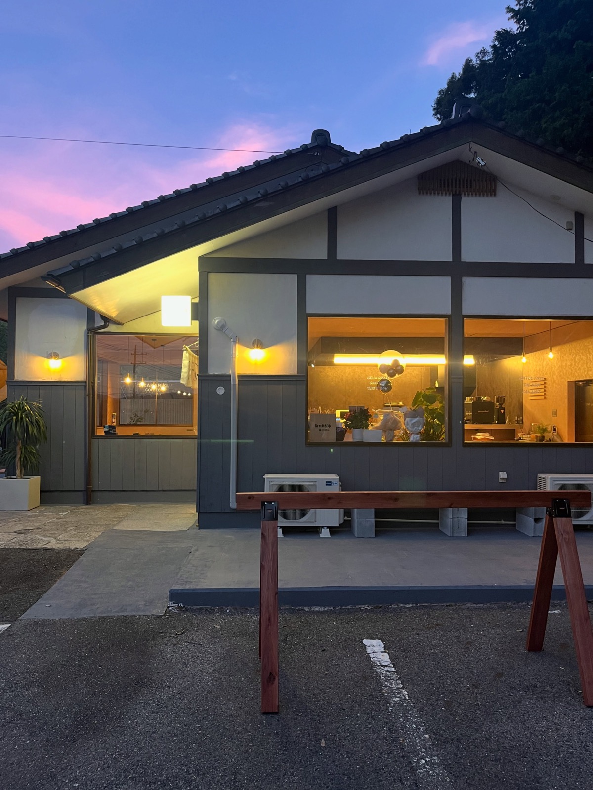 ピンク色に染まる夕暮れの空の下、瓦屋根の建物の大きな窓から温かな明かりがこぼれるSh:AKARIKI COFFEEの外観（Sh:AKARIKI COFFEE公式Instagramより）