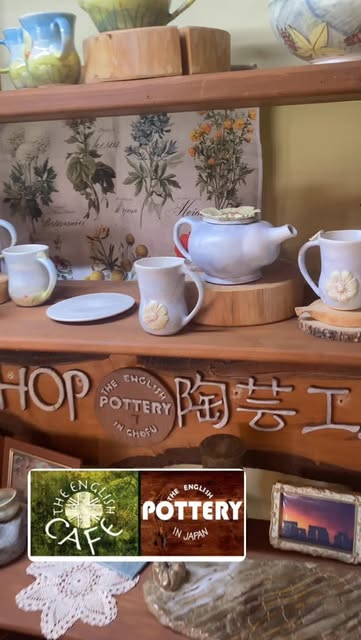 「SHOP/THE ENGLISH POTTERY IN CHOFU/陶芸工」と彫られた木の看板の上の棚に、白い花の飾りがついたティーポットやマグ、ピッチャーが並ぶ(The English Cafe公式Instagramより)