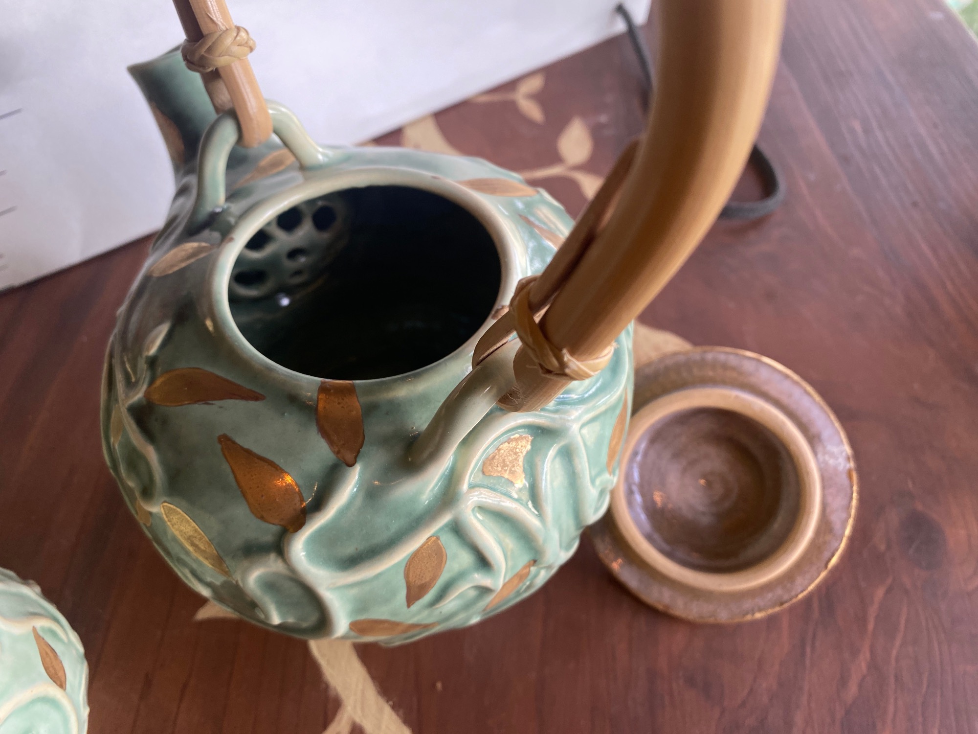 青磁釉の急須の蓋を開けたところ。表面にはアールヌーヴォー調の唐草と金彩の葉が彫り出され、竹の持ち手が付いている(The English Pottery公式サイトより)