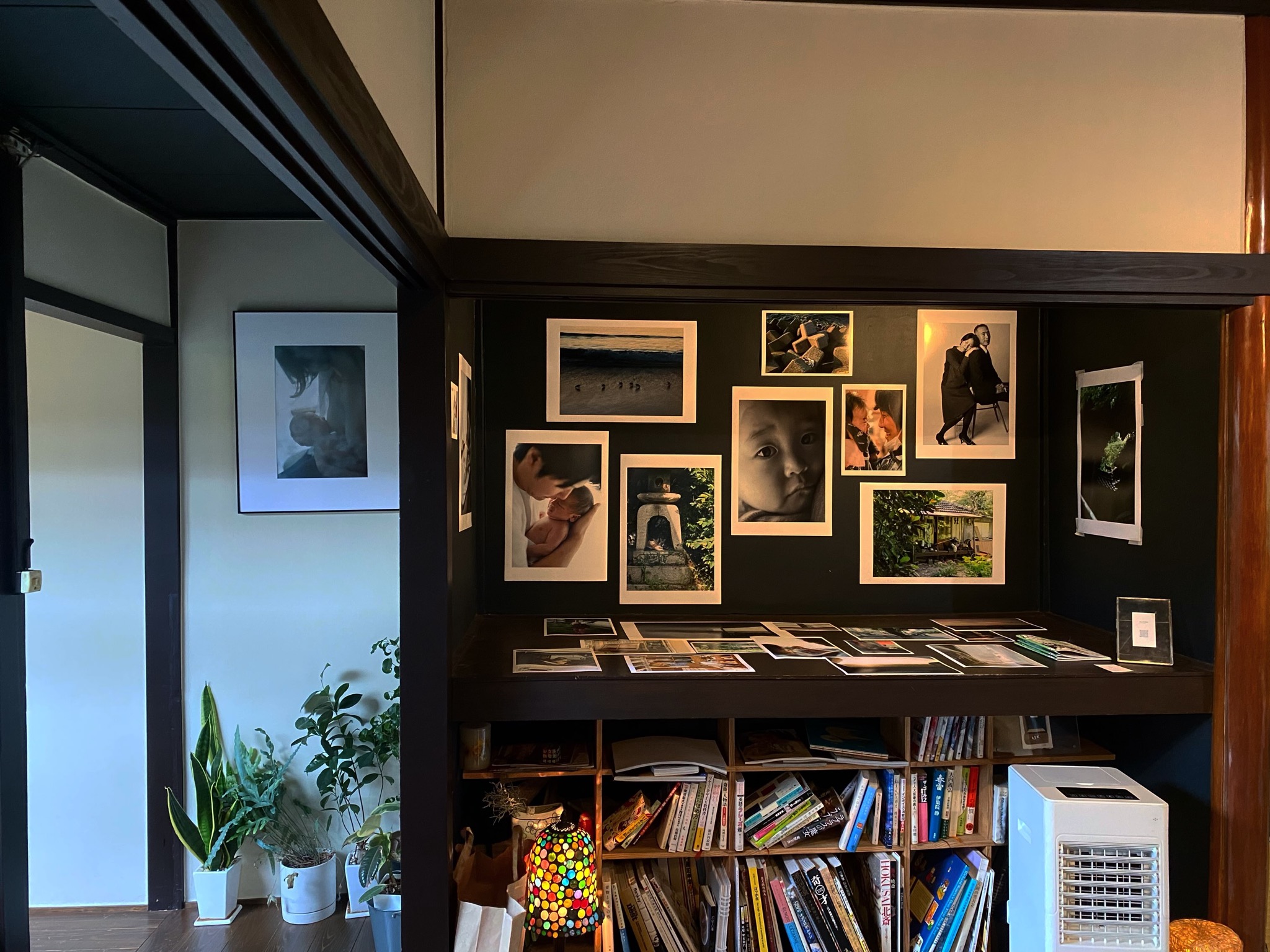 黒い壁に写真作品が並び、下の棚にはポストカードや画集、本がぎっしり並ぶGallery CAFE とこのまの店内(とこのま公式Instagramより)
