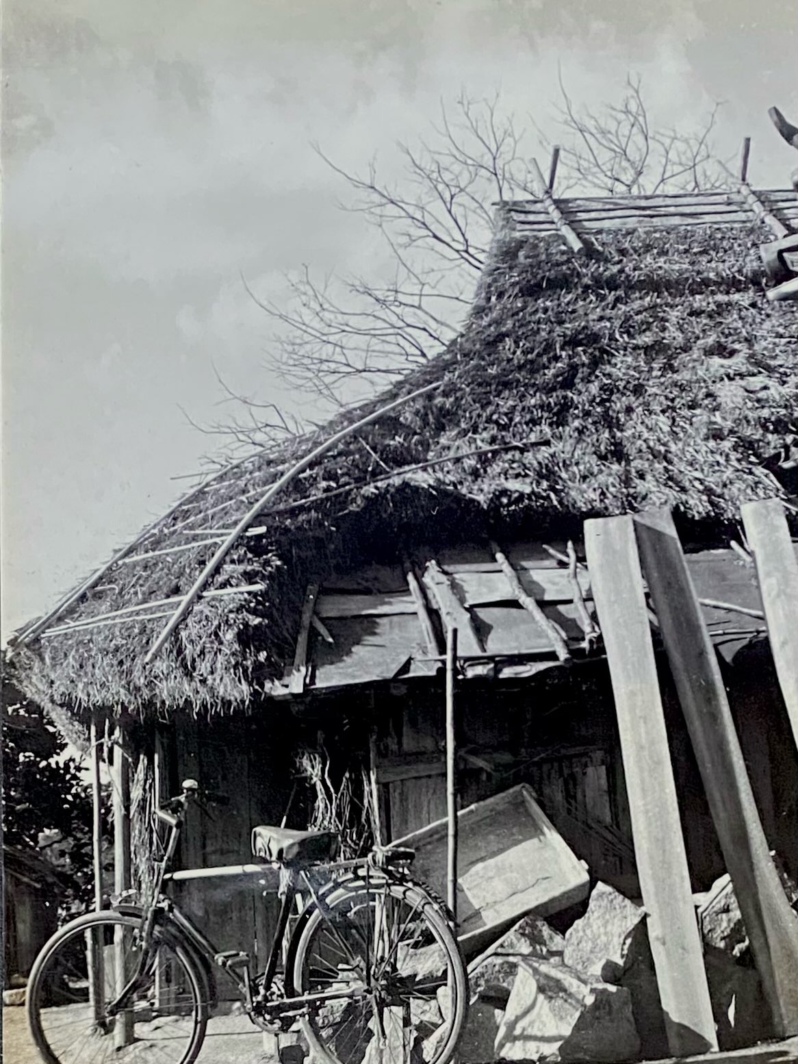 茅葺き屋根の古い家の前に自転車が停められた1930年代のモノクロ写真(Gallery CAFE とこのま公式Instagramより)