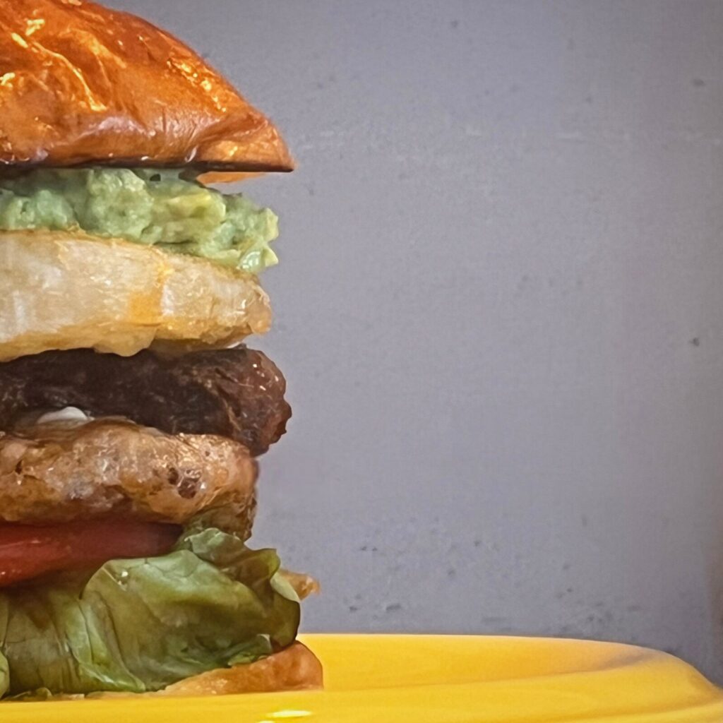 角島OZ BURGERの関門ポークパティバーガーの断面、レタスやアボカド、パティが層になった写真(公式Instagramより)