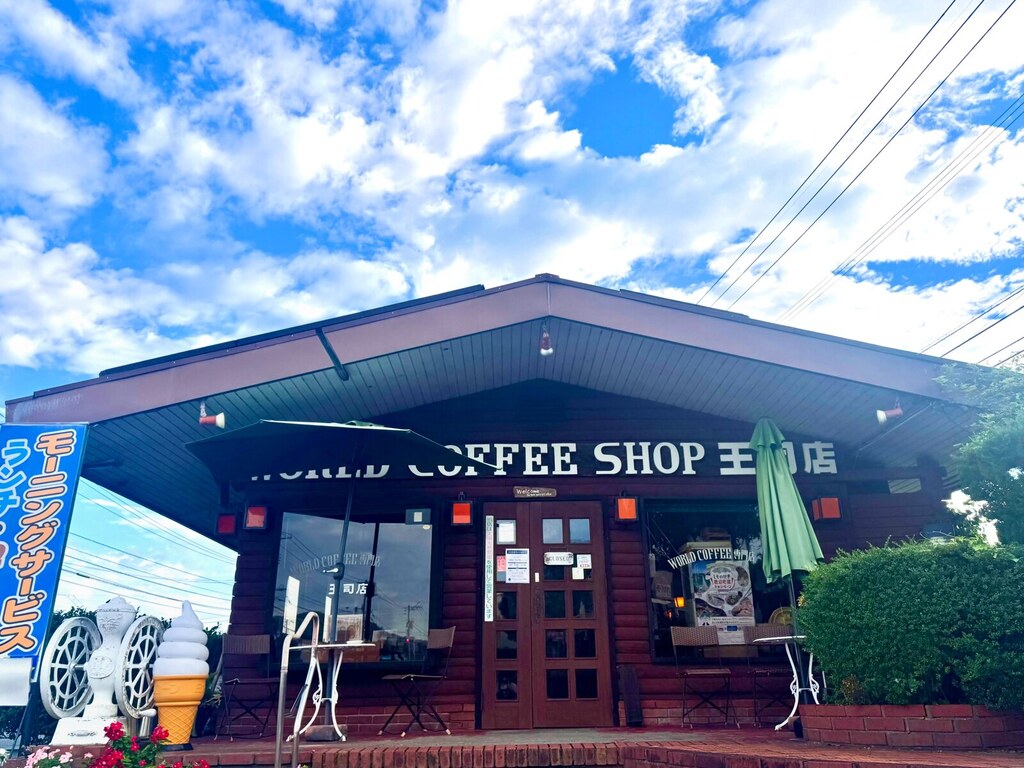 ワールドコーヒーショップ王司店の外観。ログハウス風の建物とテラス席、青空(公式Instagramより)
