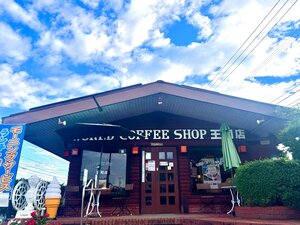 ワールドコーヒーショップ王司店の外観。ログハウス風の建物とテラス席、青空(公式Instagramより)