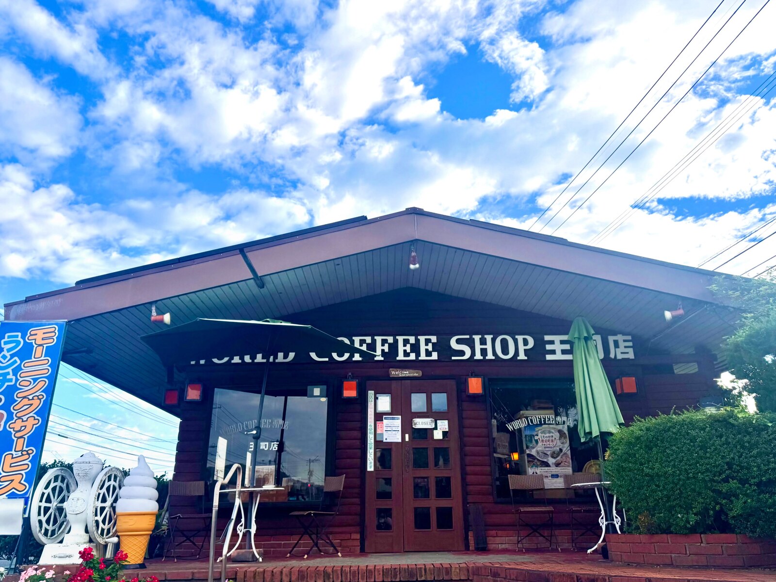 ワールドコーヒーショップ王司店の外観。ログハウス風の建物とテラス席、青空(公式Instagramより)