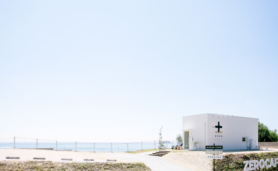 青空の下、海を背にして建つZERO CAFEの白い四角い建物と、OCEAN VIEW・TAKE OUT OK・PARKINGの看板（ZERO CAFE公式サイトより）