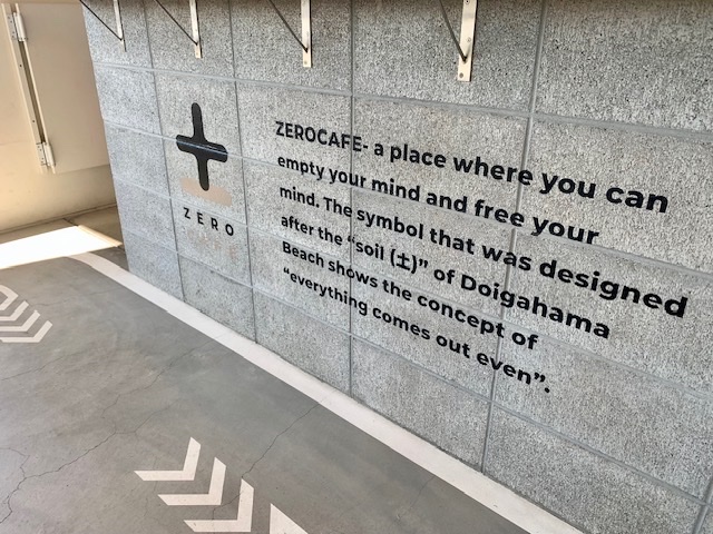 グレーの壁に描かれたZERO CAFEのプラス型ロゴと、店名の由来を説明する英文メッセージ（ZERO CAFE公式サイトより）