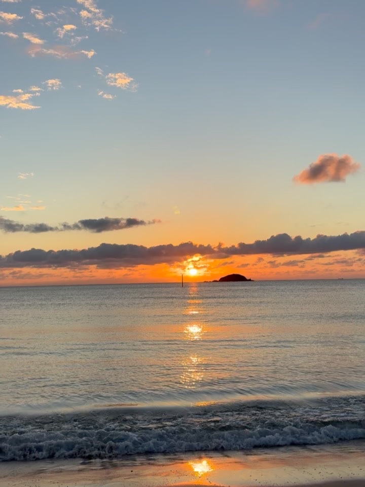 水平線に沈む夕陽と、オレンジ色に光る波打ち際、沖に浮かぶ小島（ZERO CAFE公式Instagramより）
