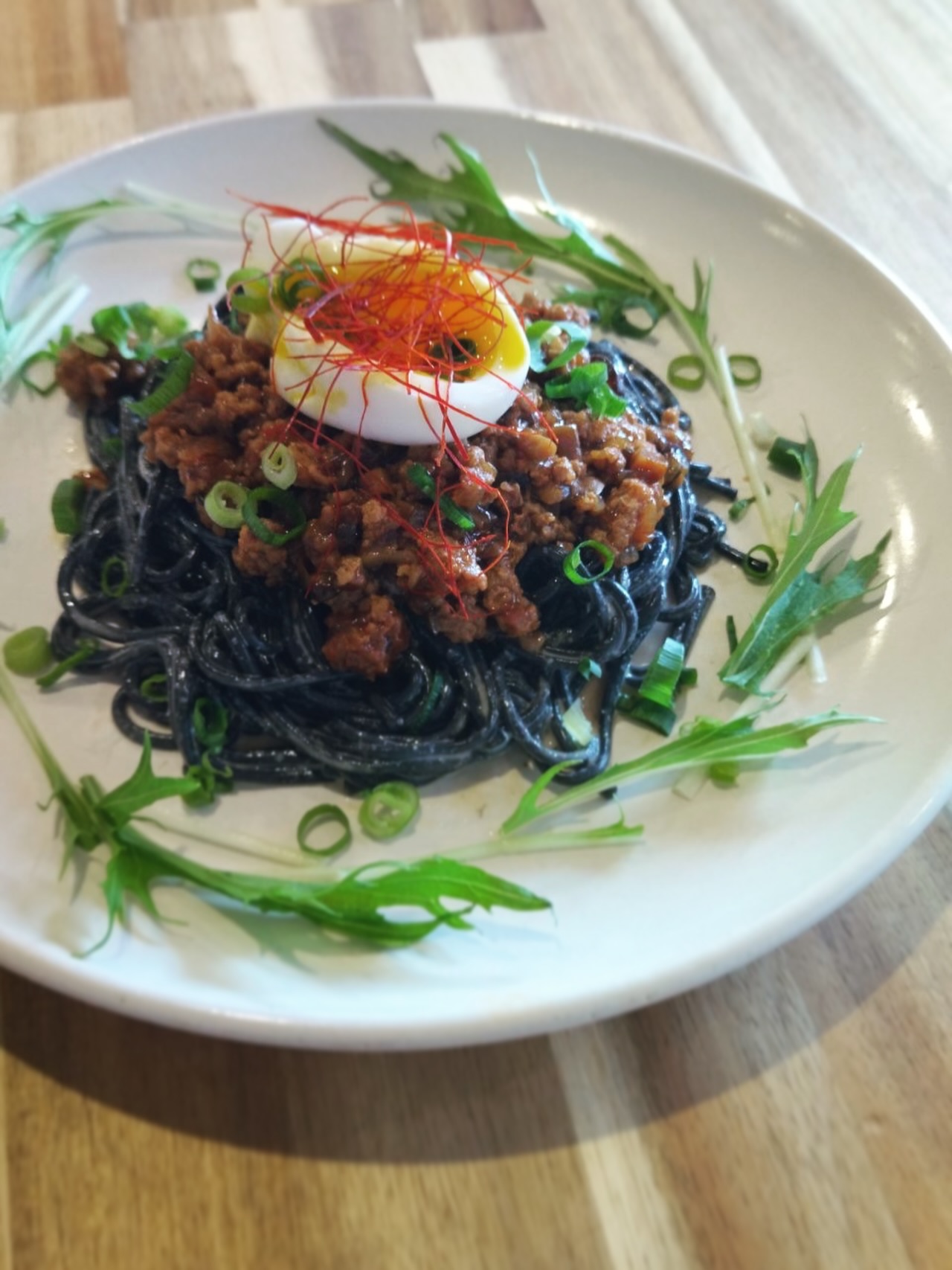 きくがわ食堂かむかむの黒ごまパスタ。ミートソースと温泉卵、水菜がトッピングされている(公式Instagramより)