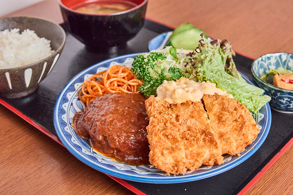 なすび食堂の看板メニュー、煮込みハンバーグ＆チキンカツ定食。ご飯・味噌汁・漬物付き(公式サイトより)